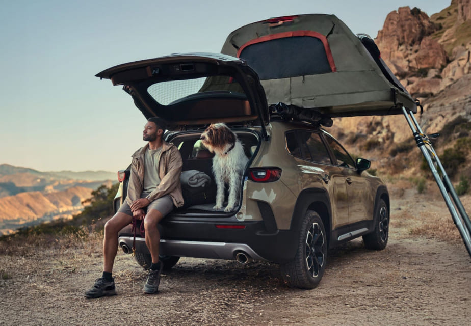Mazda CX-50 with rooftop tent, driver, and dog at a campsite