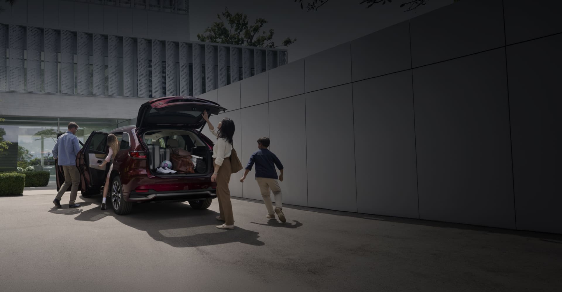 Family loading a red 2026 Mazda CX-90 outside a modern building