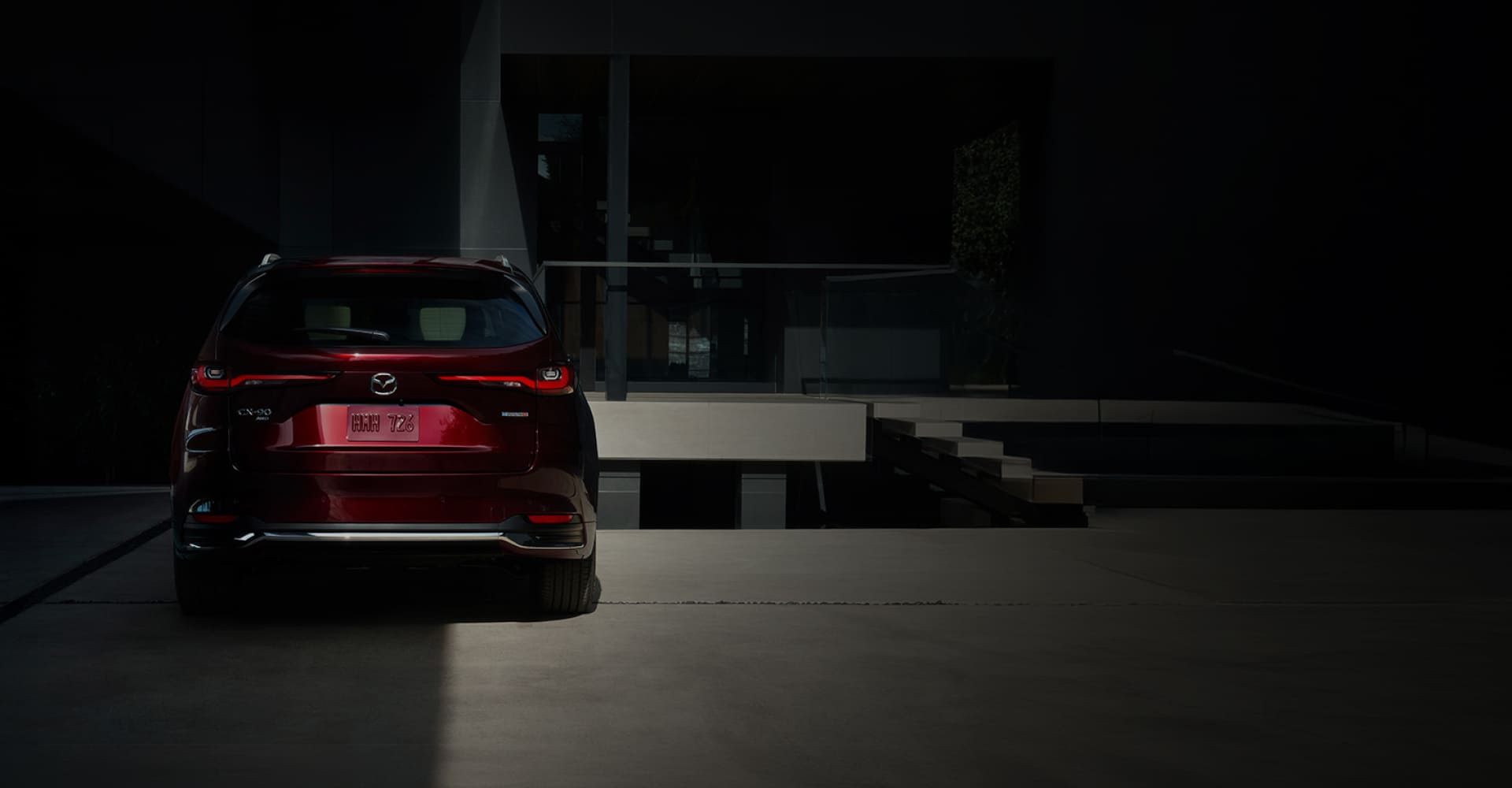 Red 2026 Mazda CX-90 viewed from behind outside a modern building