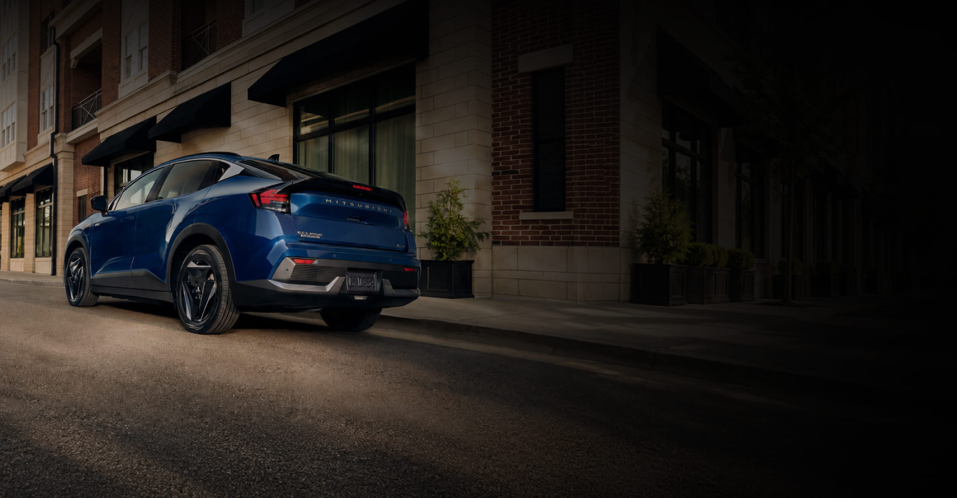 Rear three-quarter view of a blue 2027 Mitsubishi Eclipse Sportback EV parked outside a building